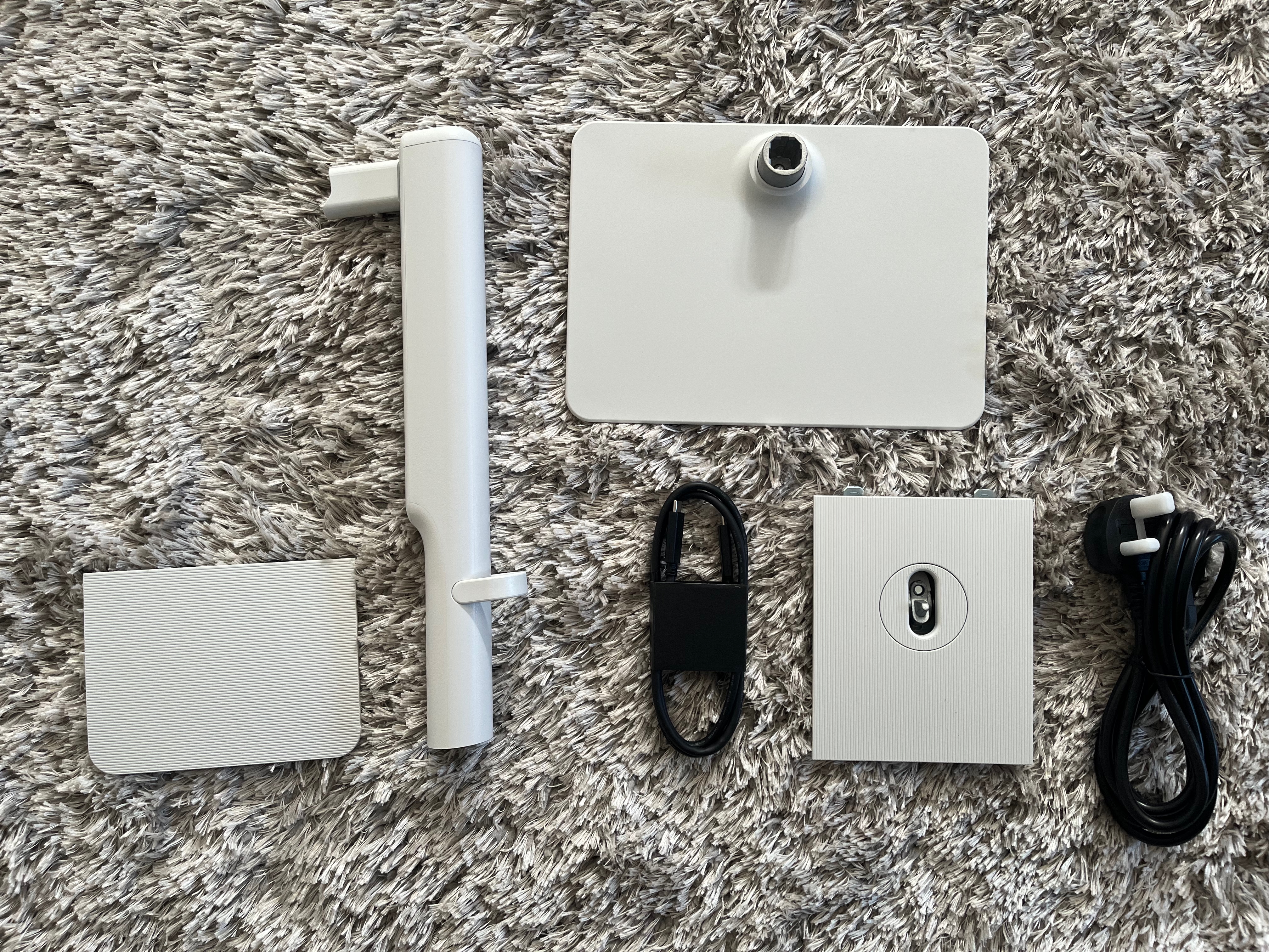 Each item described above laid out on a rug with the packaging removed. The parts for the stand and the port cover are white, while the two cables are black.