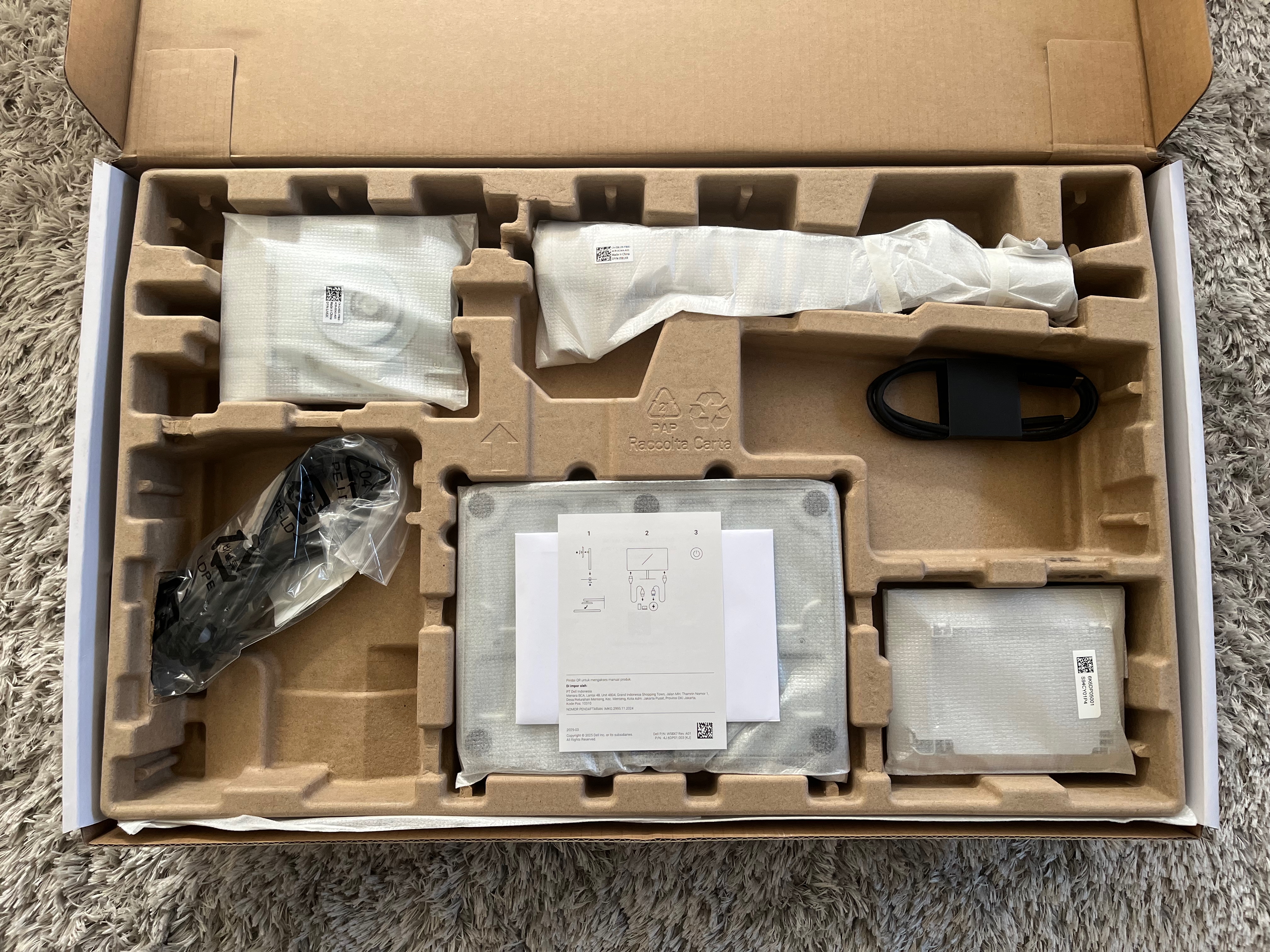 The box is open flat on the ground. Inside are the contents described below sitting on a tray, with most of it wrapped in protective foam material. Instruction papers sit on top.